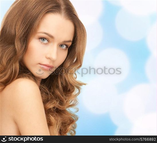 beauty, people and health concept - beautiful young woman with bare shoulders over blue lights background