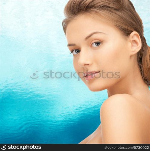 beauty, people and health concept - beautiful young woman with bare shoulders over blue water background