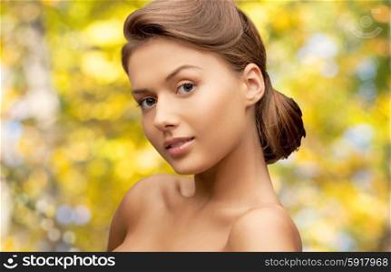 beauty, people and health concept - beautiful young woman with bare shoulders over yellow autumn background