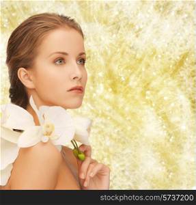 beauty, people and health concept - beautiful young woman with orchid flowers and bare shoulders over yellow lights background
