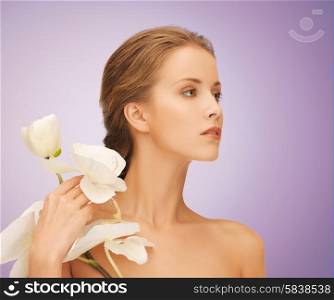beauty, people and health concept - beautiful young woman with orchid flowers and bare shoulders over violet background