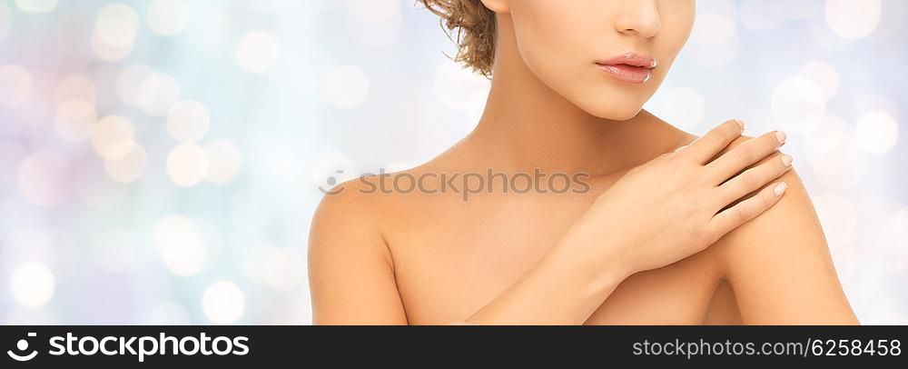 beauty, people and health concept - close up of beautiful young woman with bare shoulders over blue holidays lights background