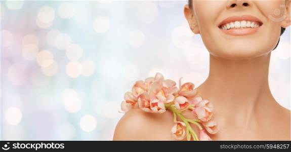 beauty, people and health concept - close up of smiling woman with orchid flower on her shoulder over blue lights background
