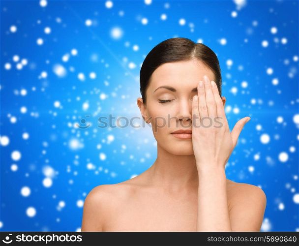 beauty, people and health concept - smiling young woman covering half of face with hand over blue snowy background
