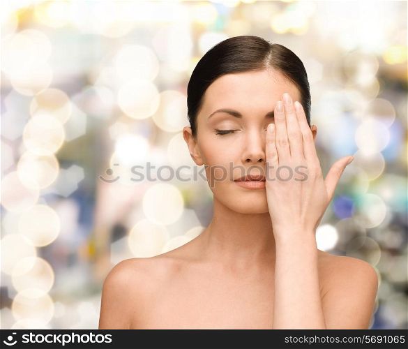 beauty, people and health concept - smiling young woman covering half of face with hand over lights background