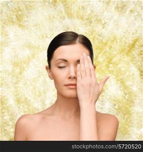 beauty, people and health concept - smiling young woman covering half of face with hand over yellow lights background