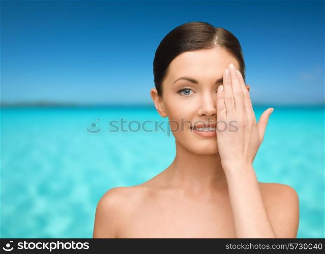 beauty, people and health concept - smiling young woman covering half of face with hand over blue sky and sea background