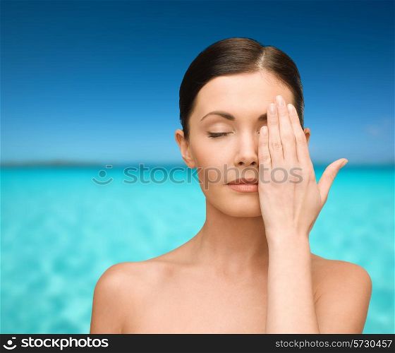 beauty, people and health concept - smiling young woman covering half of face with hand over blue sky and sea background