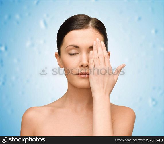 beauty, people and health concept - smiling young woman covering half of face with hand over blue wet background
