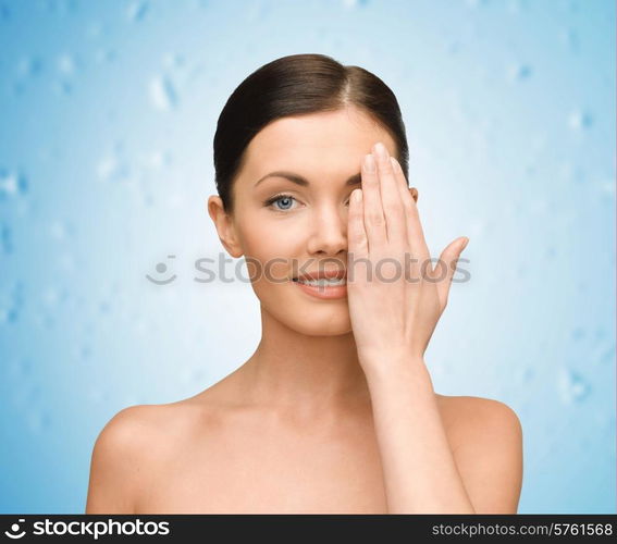 beauty, people and health concept - smiling young woman covering half of face with hand over blue wet background