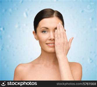 beauty, people and health concept - smiling young woman covering half of face with hand over blue wet background