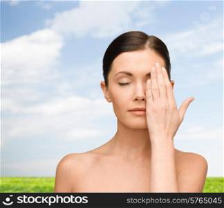beauty, people and health concept - smiling young woman covering half of face with hand over blue sky and grass background