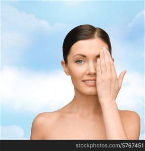 beauty, people and health concept - smiling young woman covering half of face with hand over blue sky background