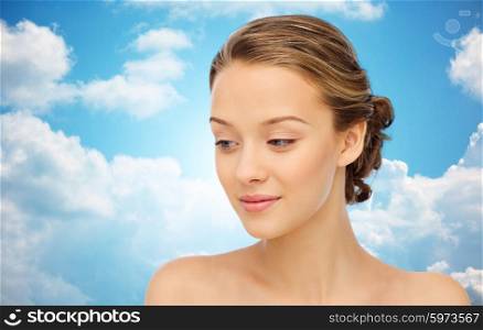 beauty, people and health concept - smiling young woman face and shoulders over blue sky and clouds background