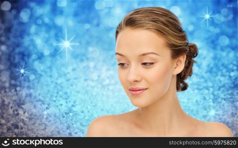 beauty, people and health concept - smiling young woman face and shoulders over blue holidays lights or glitter background