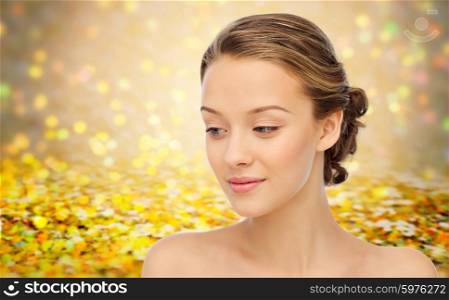 beauty, people and health concept - smiling young woman face and shoulders over golden holidays lights or yellow glitter background