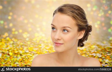 beauty, people and health concept - smiling young woman face and shoulders over yellow glitter and confetti background