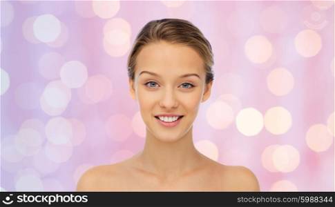 beauty, people and health concept - smiling young woman face and shoulders over pink holidays lights background