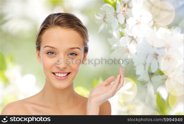 beauty, people and health concept - smiling young woman face and shoulders over summer green natural background with cherry blossom