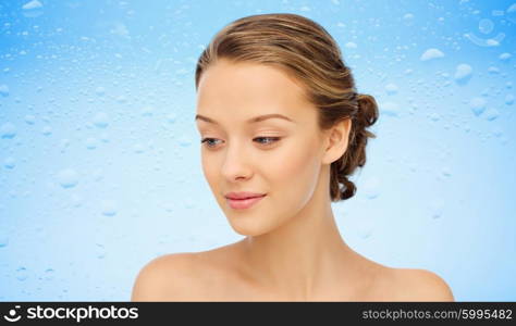 beauty, people and health concept - smiling young woman face and shoulders over water drops on blue background