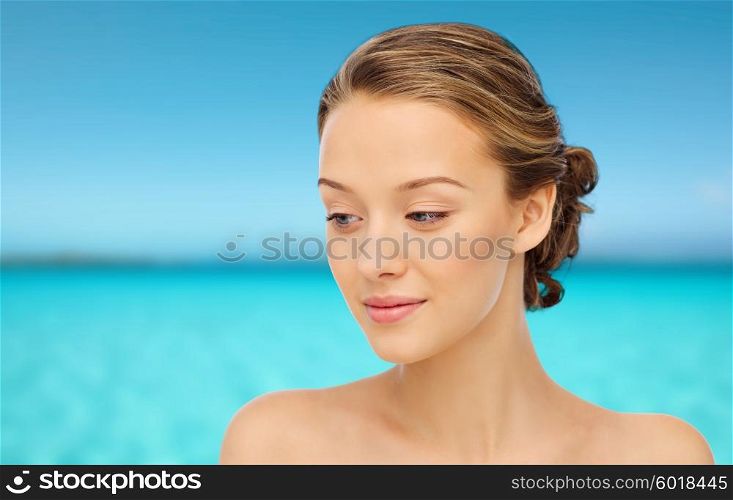 beauty, people and health concept - smiling young woman face and shoulders over blue sea and sky background