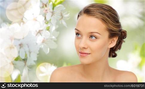 beauty, people and health concept - smiling young woman face and shoulders over green natural cherry blossom background