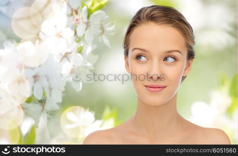 beauty, people and health concept - smiling young woman face and shoulders over summer green natural background with cherry blossom