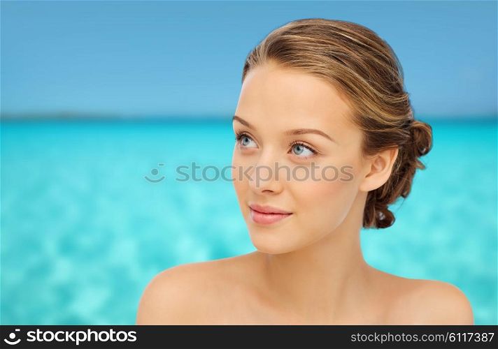 beauty, people and health concept - smiling young woman face and shoulders over blue sea and sky background