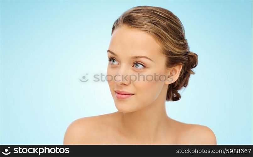 beauty, people and health concept - smiling young woman face and shoulders over blue background