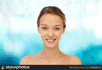 beauty, people and health concept - smiling young woman face and shoulders over blue water background