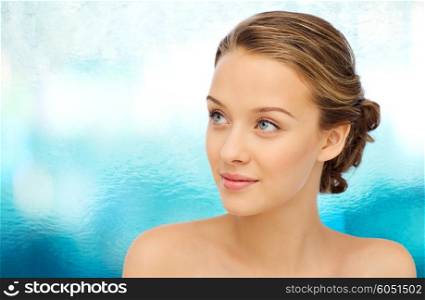 beauty, people and health concept - smiling young woman face and shoulders over blue water background