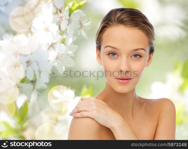 beauty, people and health concept - smiling young woman face and shoulders over cherry blossom background