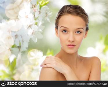 beauty, people and health concept - smiling young woman face and shoulders over cherry blossom background