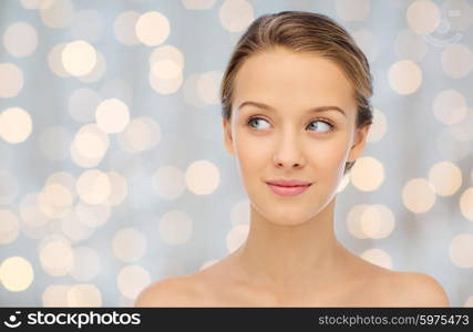 beauty, people and health concept - smiling young woman face and shoulders over holidays lights background