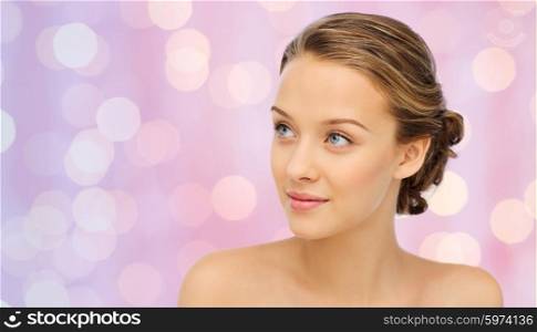 beauty, people and health concept - smiling young woman face and shoulders over pink lights background