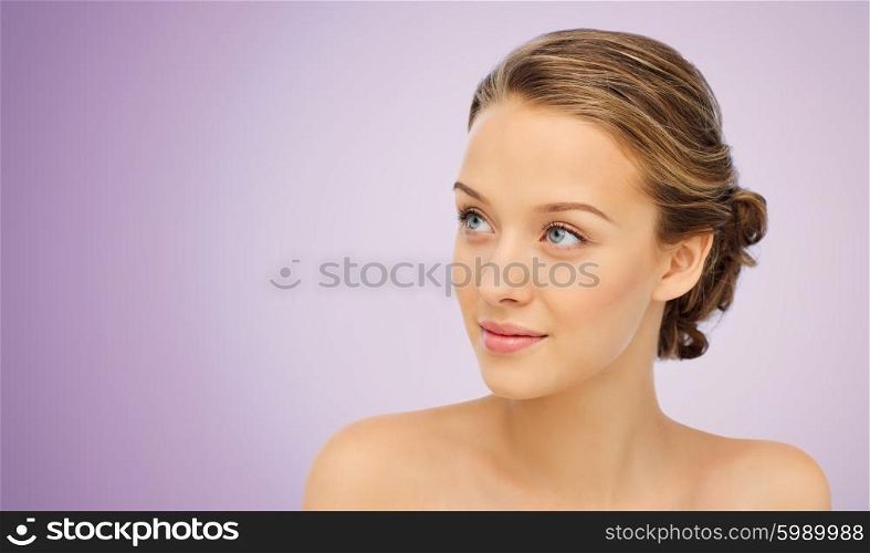 beauty, people and health concept - smiling young woman face and shoulders over violet background