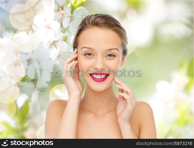 beauty, people and health concept - smiling young woman face with pink lipstick on lips and shoulders over green natural background with cherry blossoms