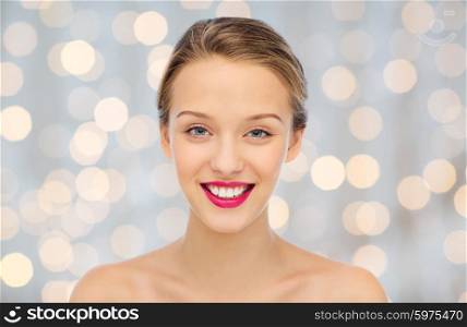 beauty, people and health concept - smiling young woman face with pink lipstick on lips and shoulders over holidays lights background