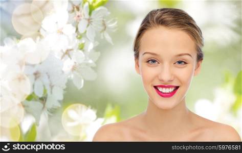 beauty, people and health concept - smiling young woman face with pink lipstick on lips and shoulders over summer green natural background with cherry blossom