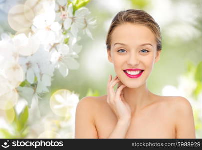 beauty, people and health concept - smiling young woman face with pink lipstick on lips and shoulders over green natural cherry blossom background