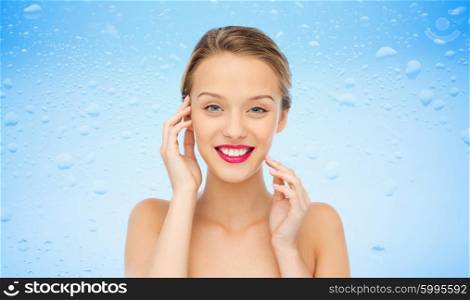 beauty, people and health concept - smiling young woman face with pink lipstick on lips and shoulders over water drops on blue background