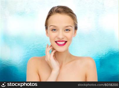 beauty, people and health concept - smiling young woman face with pink lipstick on lips and shoulders over blue water background