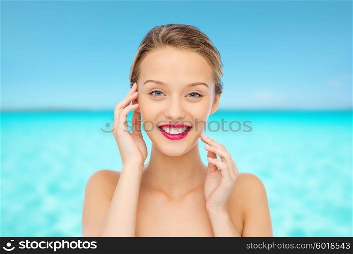beauty, people and health concept - smiling young woman face with pink lipstick on lips and shoulders over blue sea and sky background