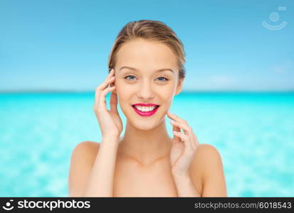 beauty, people and health concept - smiling young woman face with pink lipstick on lips and shoulders over blue sea and sky background