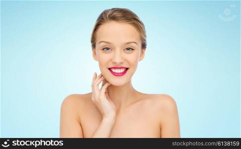 beauty, people and health concept - smiling young woman face with pink lipstick on lips and shoulders over blue background