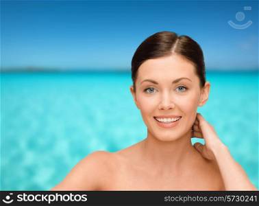 beauty, people and health concept - smiling young woman with bare shoulders over blue sky and sea background