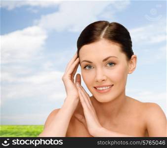 beauty, people and health concept - smiling young woman with bare shoulders over blue sky and grass background