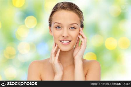 beauty, people and health concept - smiling young woman with bare shoulders touching her face over green lights background