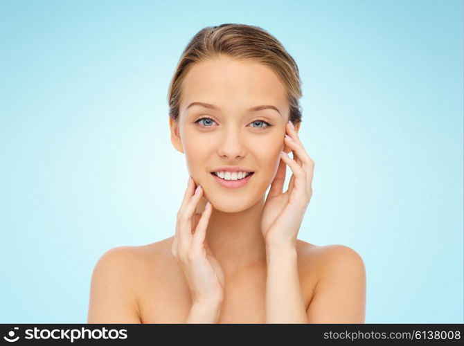 beauty, people and health concept - smiling young woman with bare shoulders touching her face over blue background