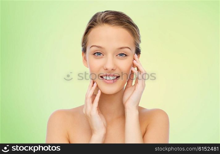 beauty, people and health concept - smiling young woman with bare shoulders touching her face over green natural background